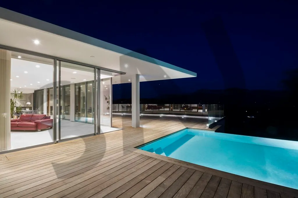 Séjour éclairé vu depuis la piscine, de nuit